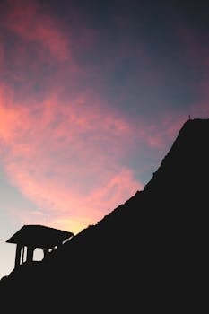 Silhouetted mountain and structure against a colorful sunset sky in Lugano, Switzerland.