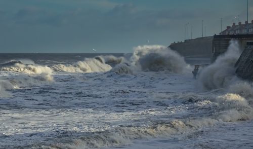 Free Powerful ocean waves crash against a seawall under a cloudy sky, showcasing nature's force. Stock Photo