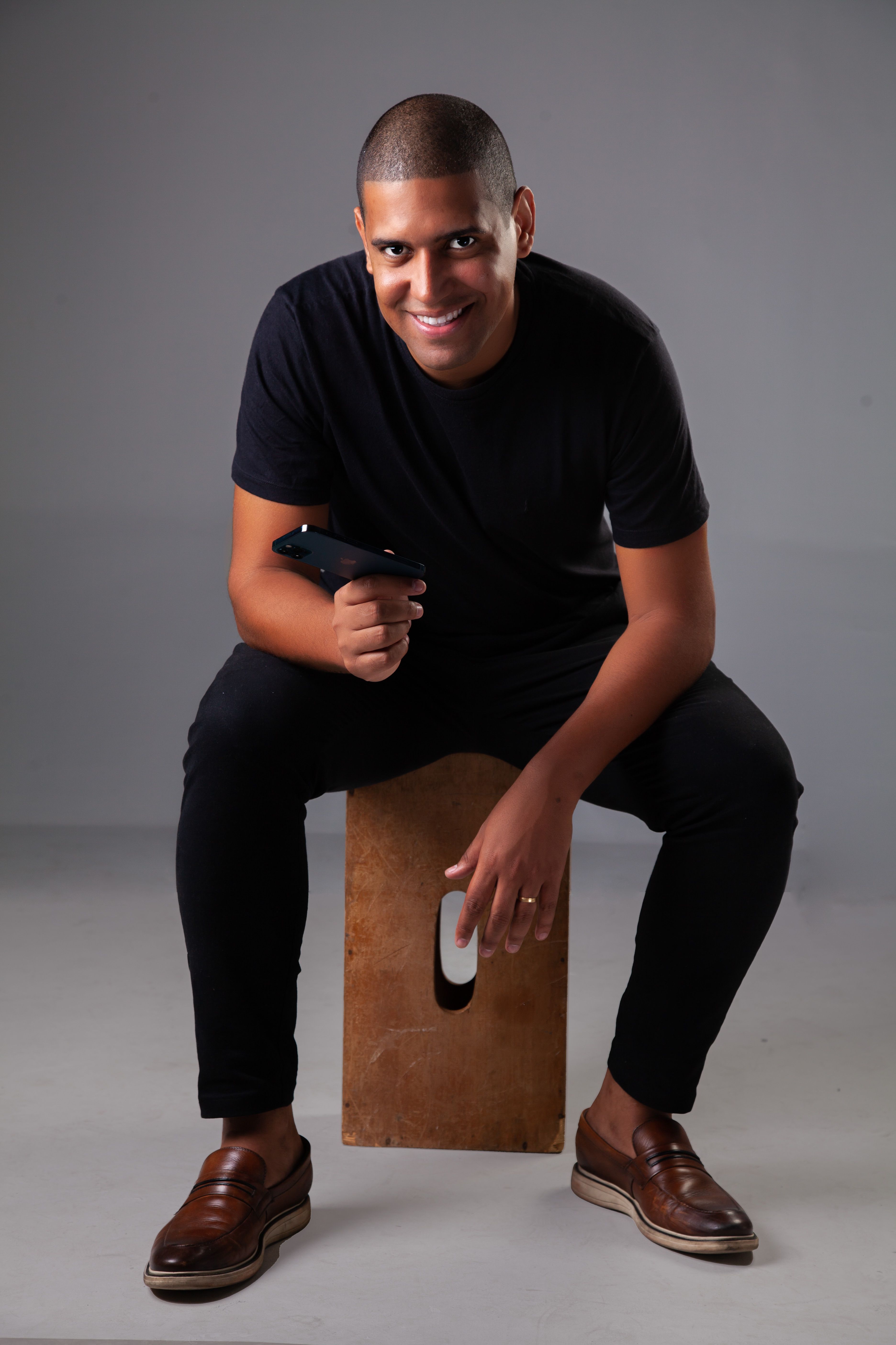Friendly man in black outfit sitting on a bench, smiling warmly at the camera. Perfect for stock images.