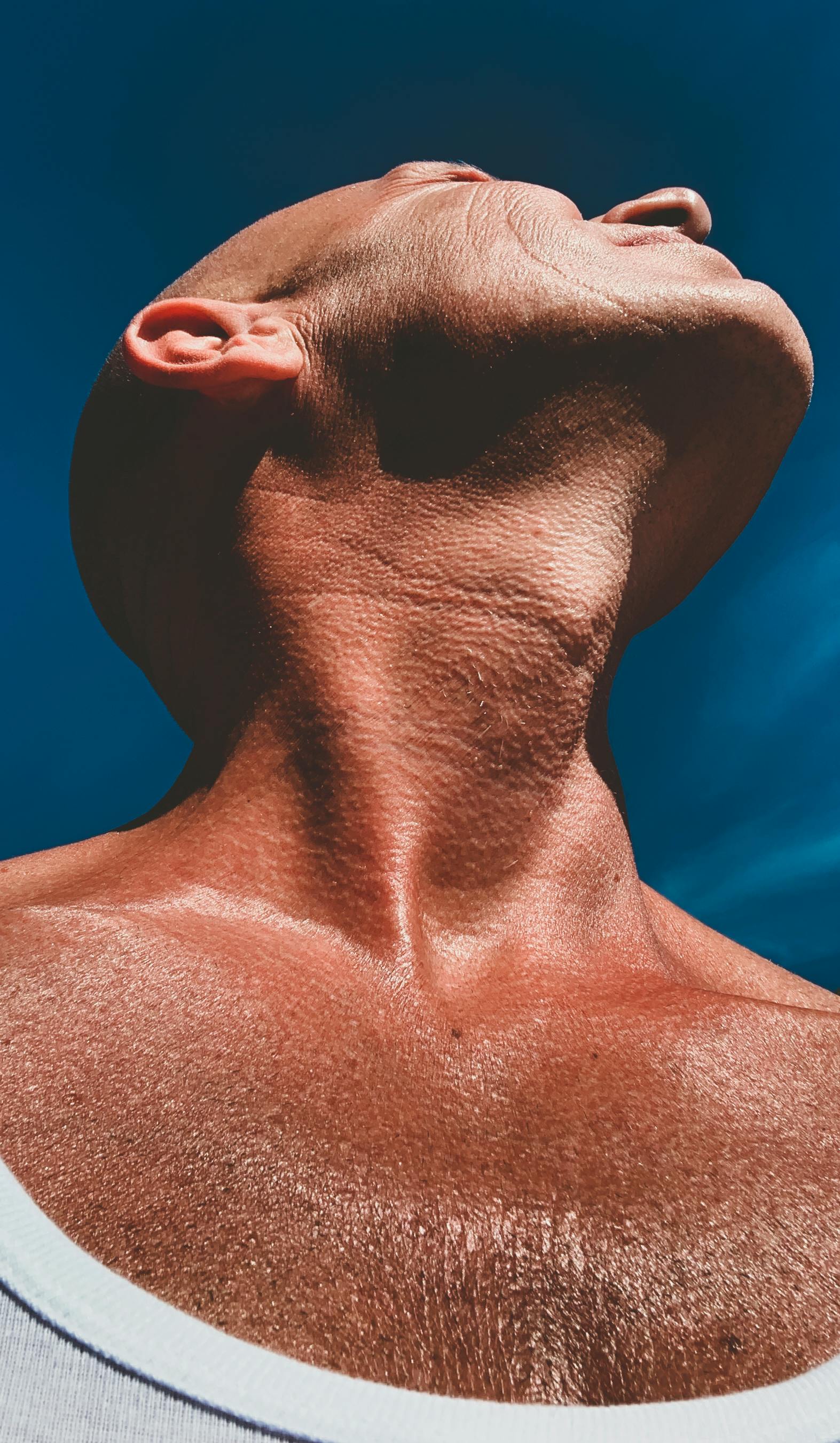 Low angle close-up of a bald man's neck and face against a blue sky, conveying strength and vitality.