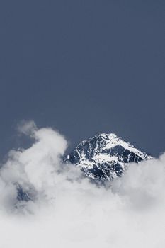 A dramatic view of a snow-capped mountain peak piercing through clouds against a dark sky.