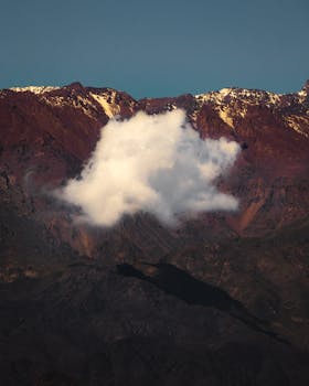 Breathtaking view of snow-capped rugged mountains under a clear blue sky with a solitary cloud.
