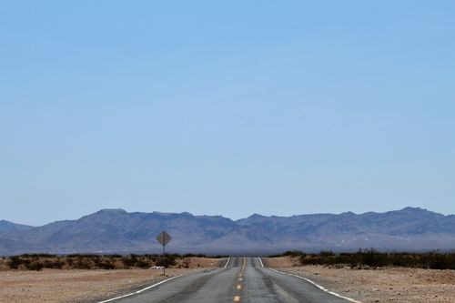 Free Empty road stretching towards distant mountains under clear blue skies. Stock Photo