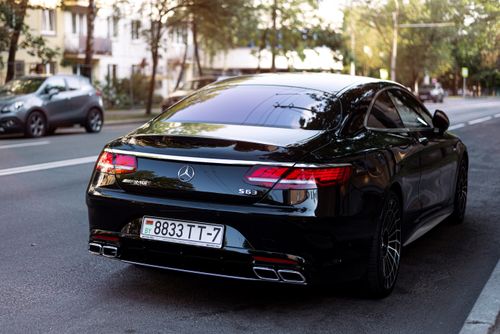 Free Sleek black luxury car parked on a city street with sunlight reflecting off its surface. Stock Photo