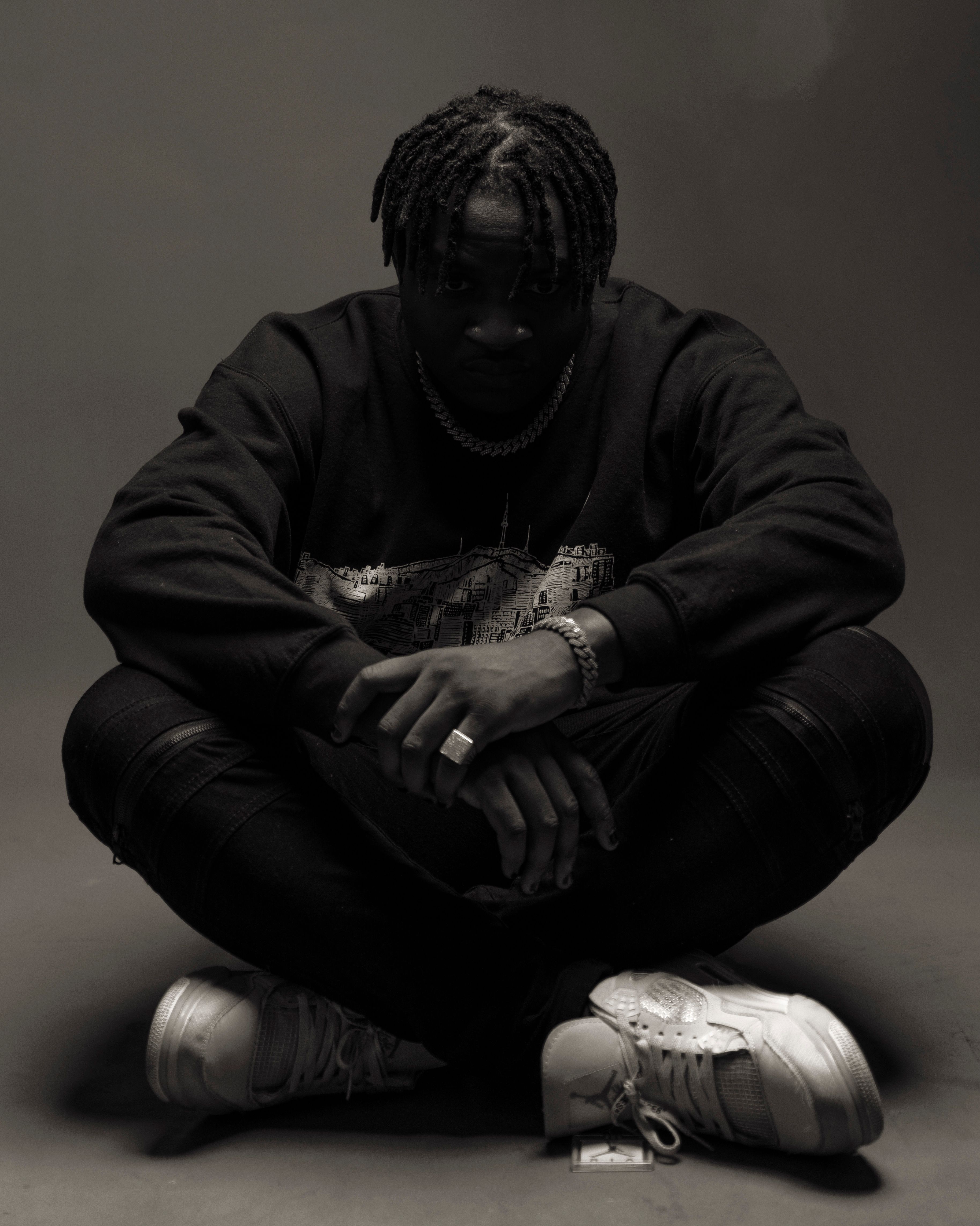 Monochrome portrait of a stylish man sitting cross-legged in a Lagos studio setting.