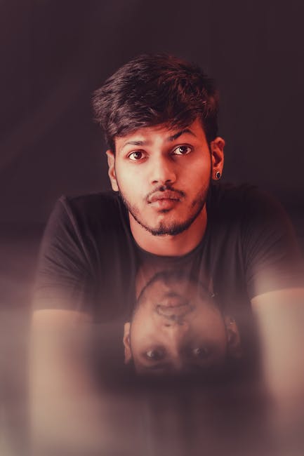 Close-up portrait of a young South Asian man with a reflection on a dark background.