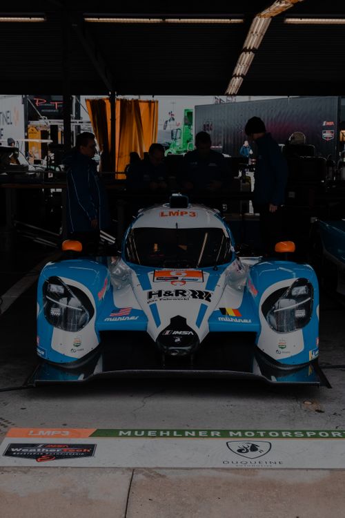 Free Close-up of a racing car in a pit garage setting with crew members. Stock Photo