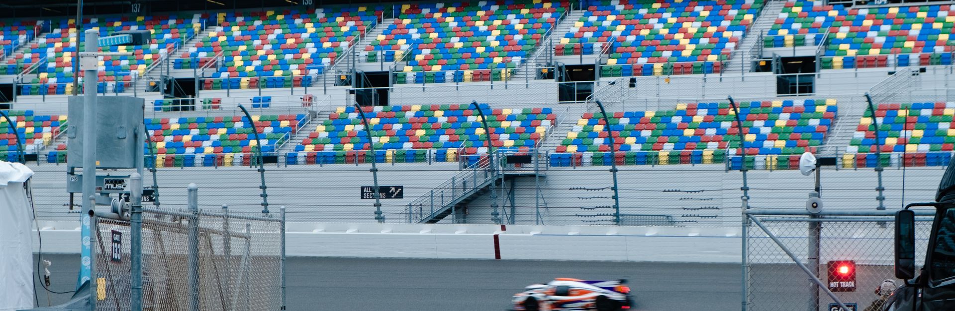 Blurred race car speeding past colorful bleachers at a famous track.
