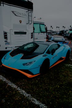 A striking blue and orange sports car parked beside a luxury RV on a grassy lot.