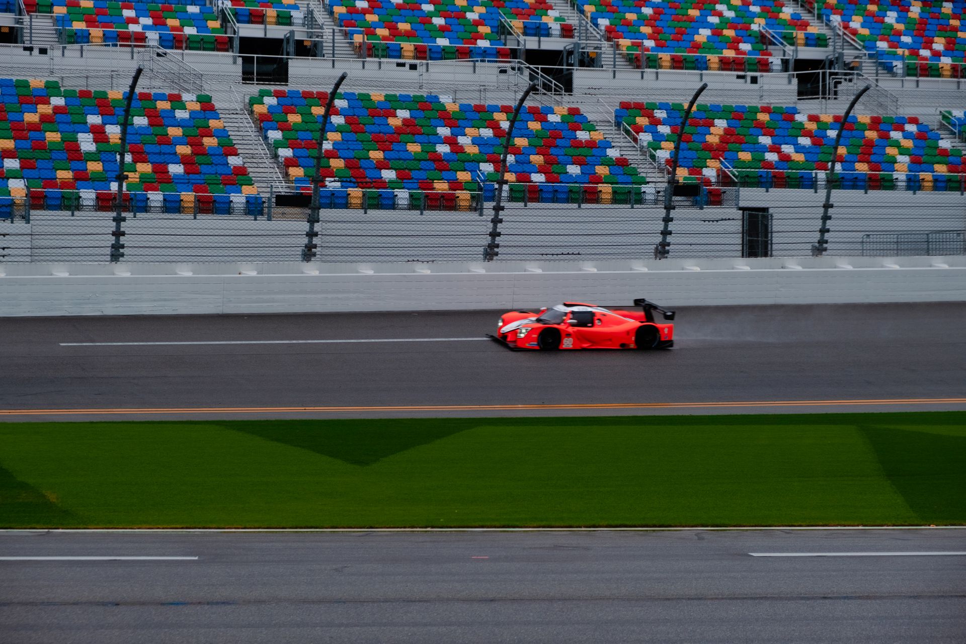 A vibrant red race car speeding on a track with empty colorful stands in the background.