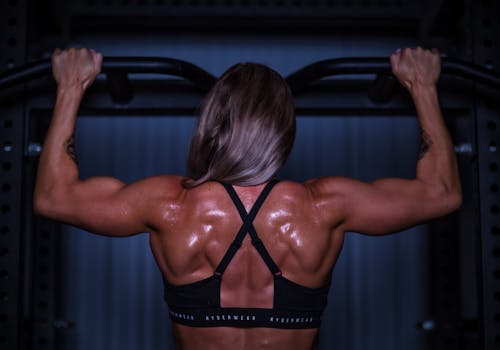 A female bodybuilder showcasing strength and muscle definition during a pull-up workout.