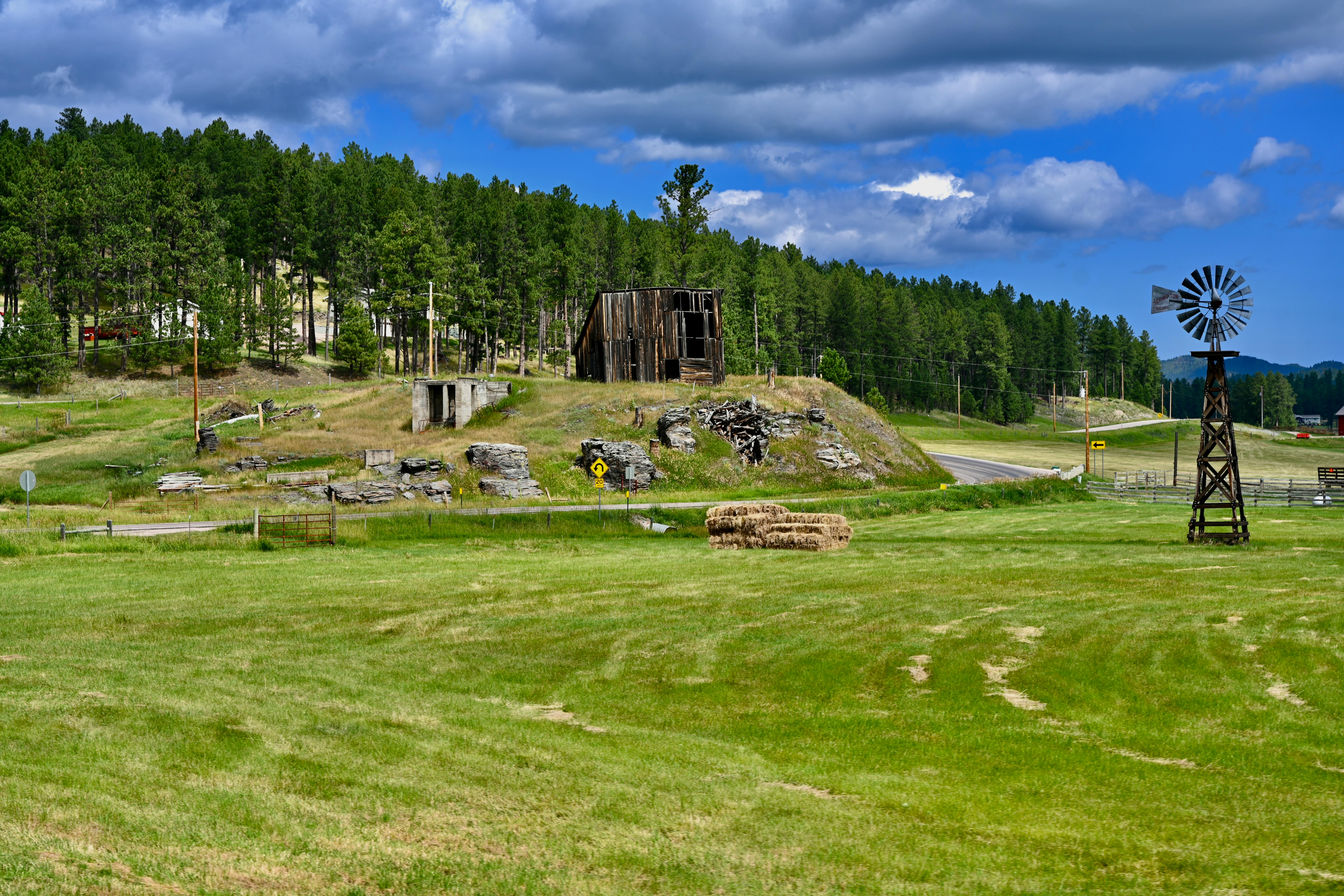 Scenic countryside featuring an old barn, windmill, and lush green fields under a blue sky.