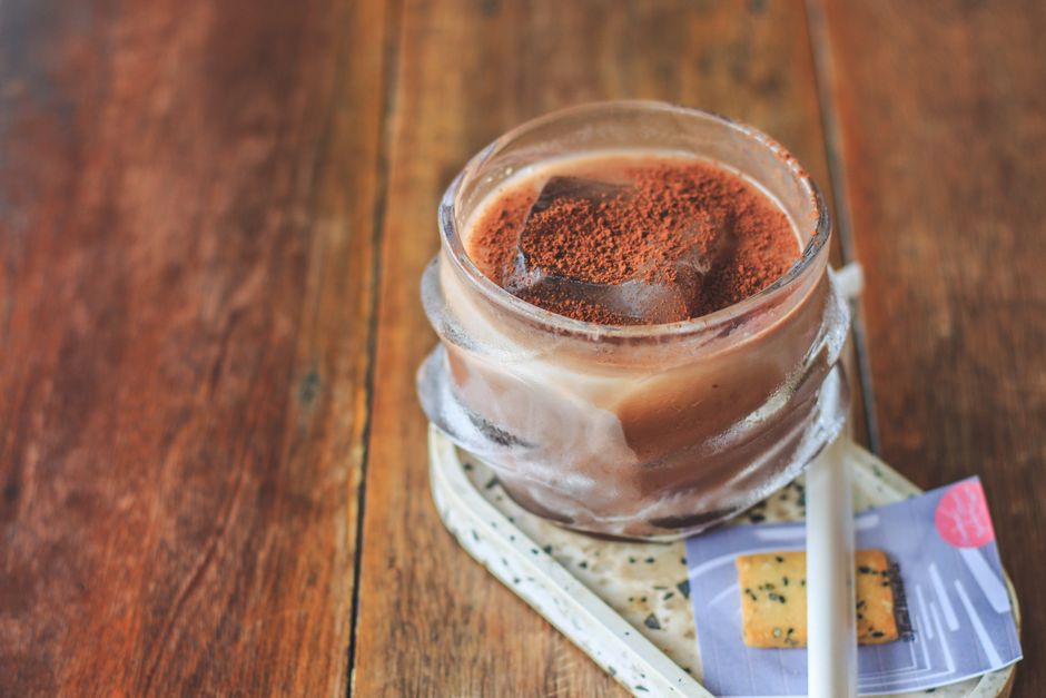 Refreshing iced chocolate drink with cocoa powder and ice cubes in a glass cup on a rustic wooden table.