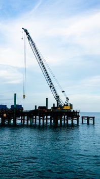 A large crane operating at sea on a pier for cargo operations under a cloudy sky.
