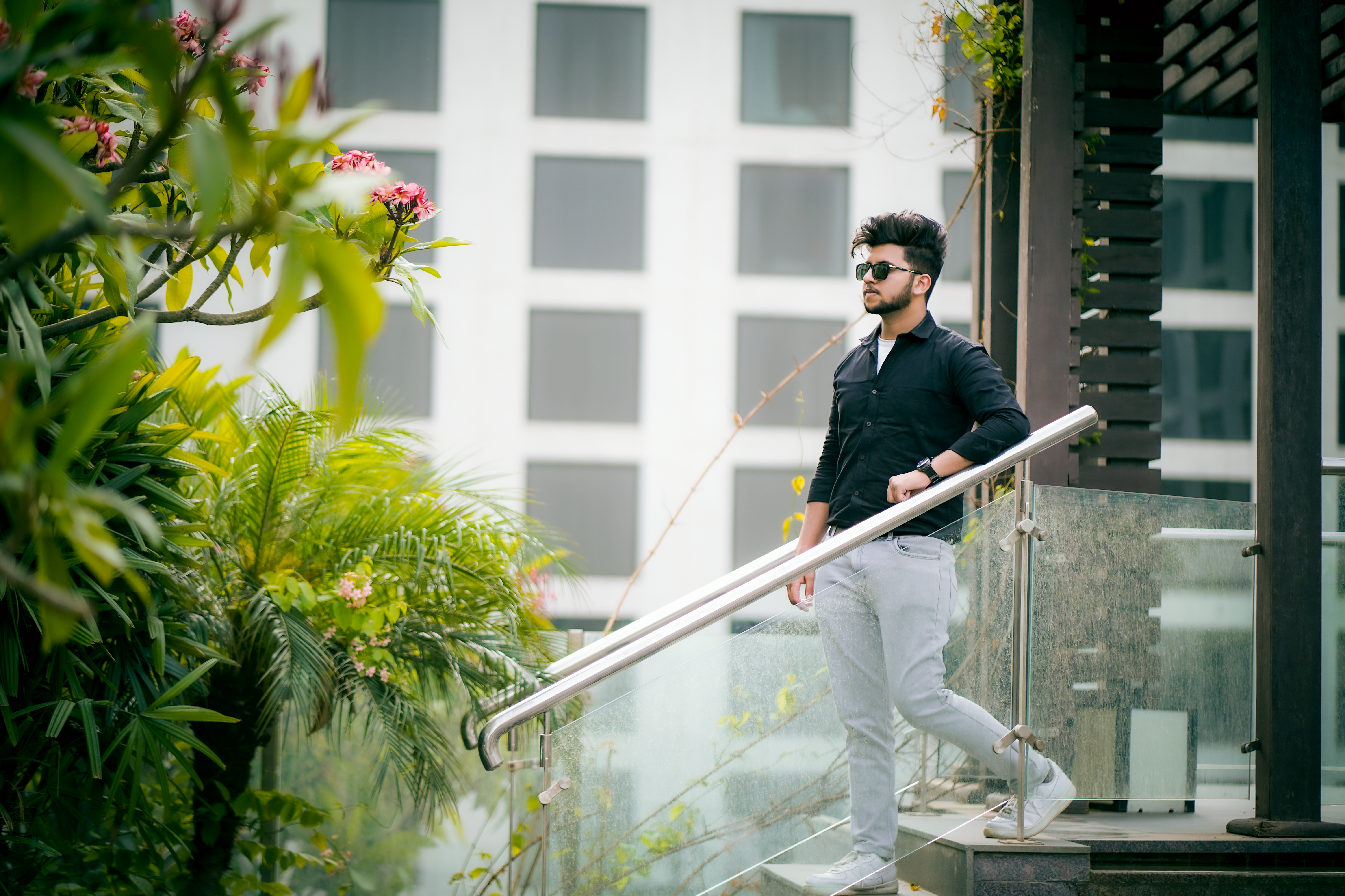 Fashionable man in black and white attire posing on outdoor stairs with lush greenery.