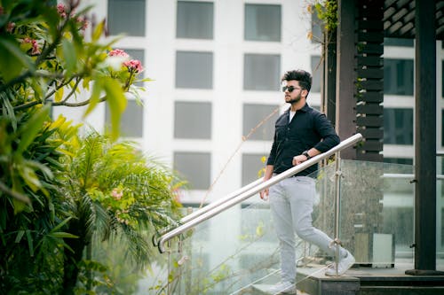 Man in Black Long Sleeve Shirt and White Pants Standing on the Stairs