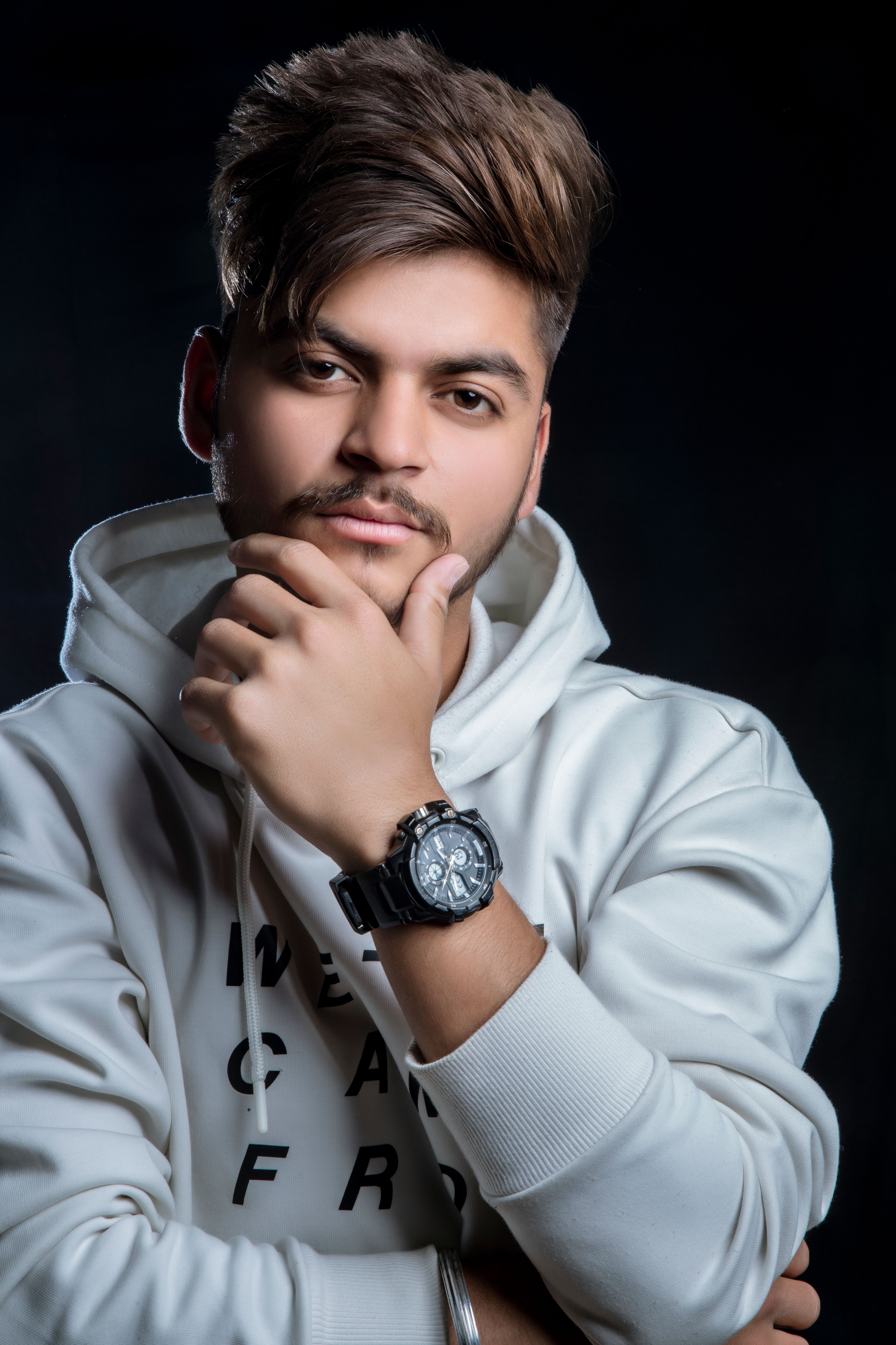 Young man in a white hoodie posing confidently in a studio setting. Perfect for fashion and lifestyle themes.