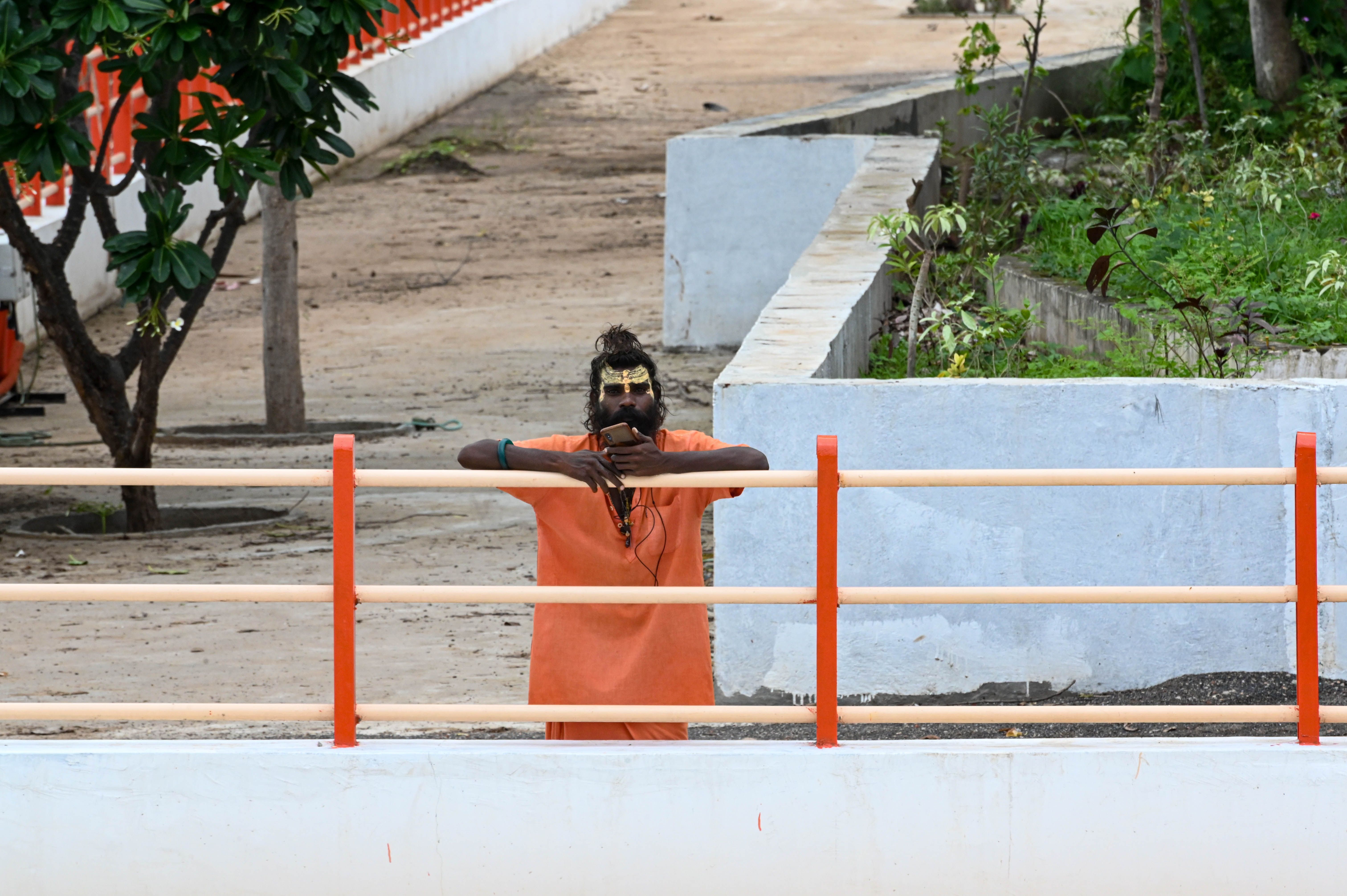 A Hindu sadhu in orange robes standing behind a fence outdoors.
