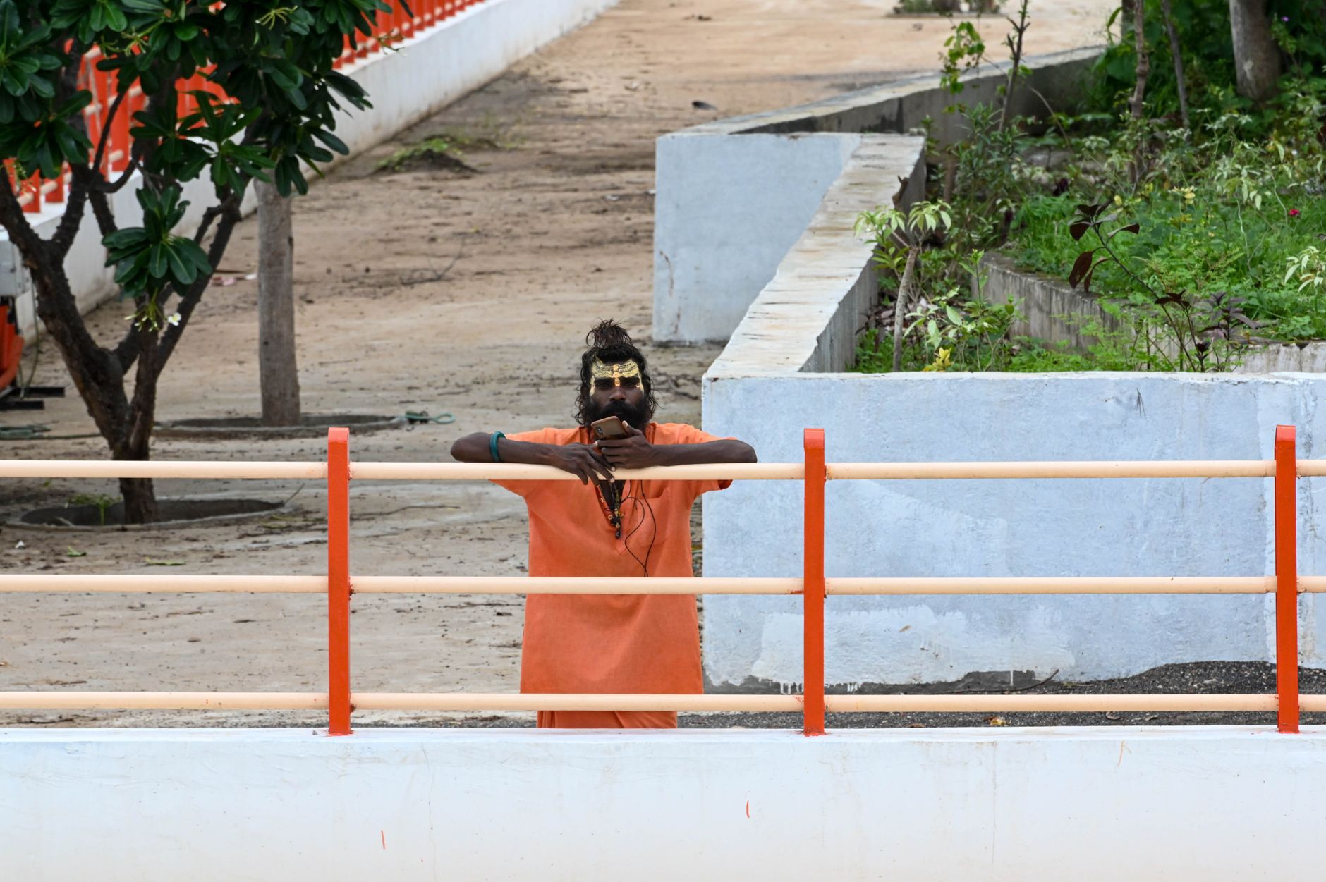 A Hindu sadhu in orange robes standing behind a fence outdoors.