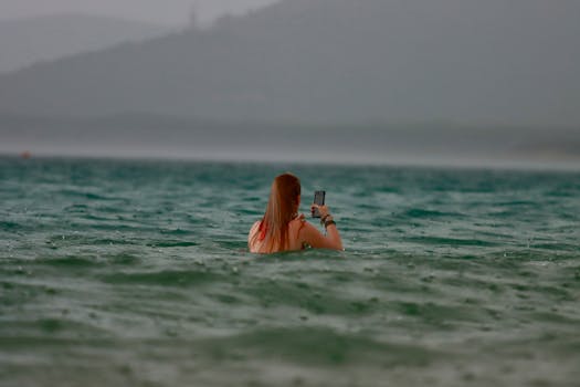 A woman takes a selfie while swimming in Alghero, Sardinia during a rain shower.