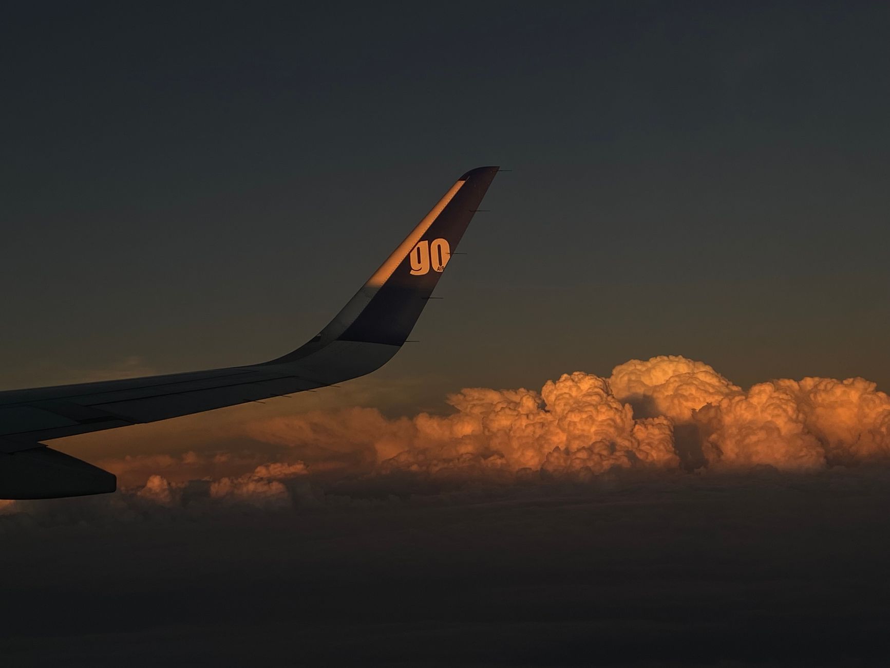A serene view from an airplane wing during sunrise, with clouds glowing in dawn light.