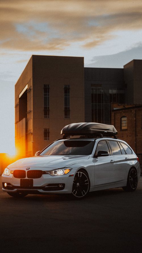 Free A white sports car with roof box parked in an urban location during sunset, showcasing modern architecture. Stock Photo