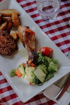 Roasted chicken leg with potatoes and fresh salad on a checkered table setting.