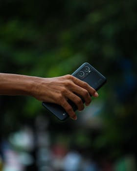 A person's hand holding a smartphone with a blurred outdoor background, focused view.