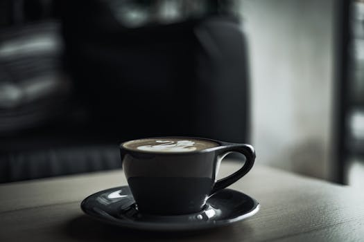 Artistic shot of a black coffee cup with latte art on a wooden table in a moody setting.