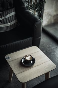 A black cup of cappuccino with latte art on a wooden table in a cozy indoor café setting.