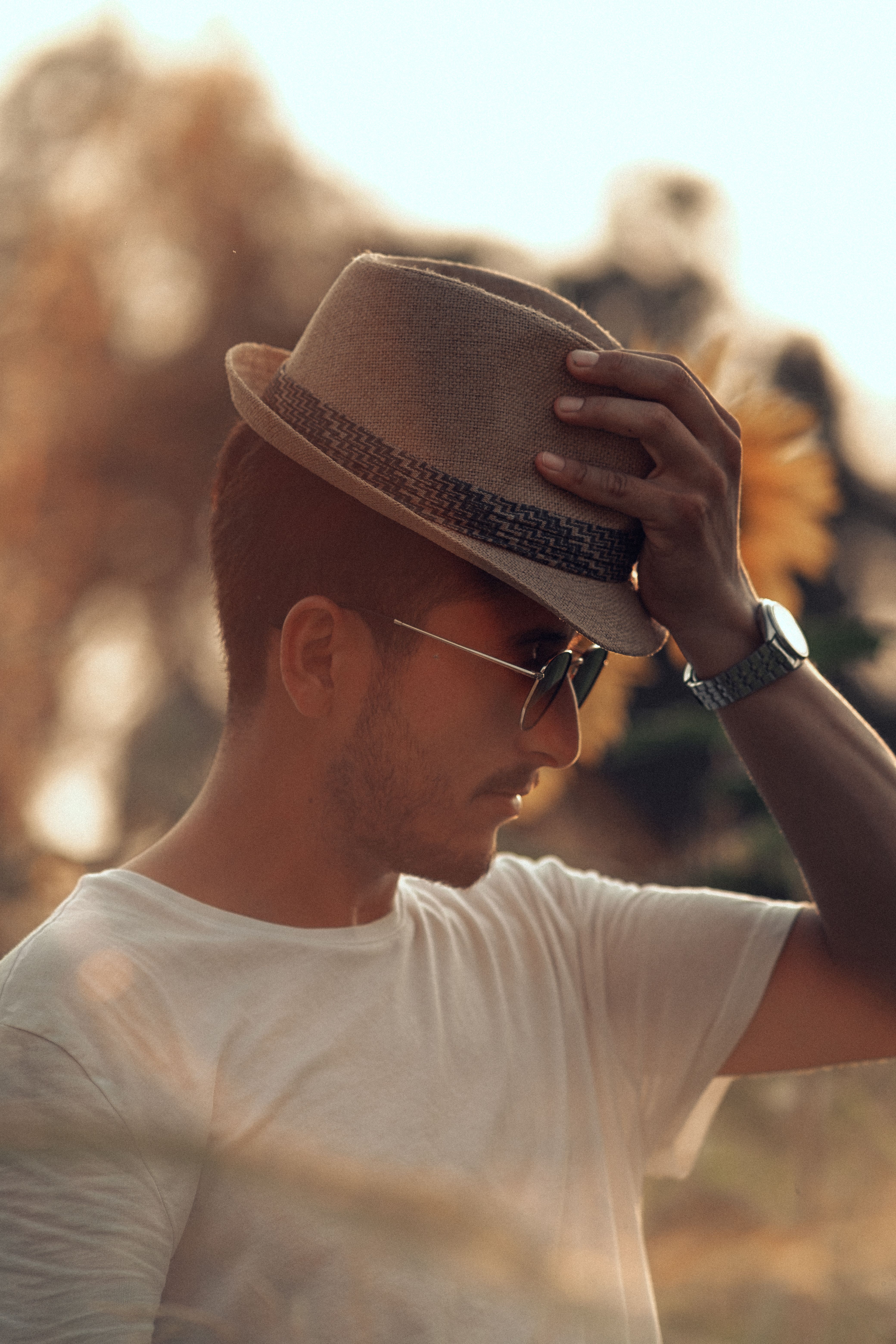 A stylish man wearing a fedora and sunglasses, captured outdoors during golden hour.