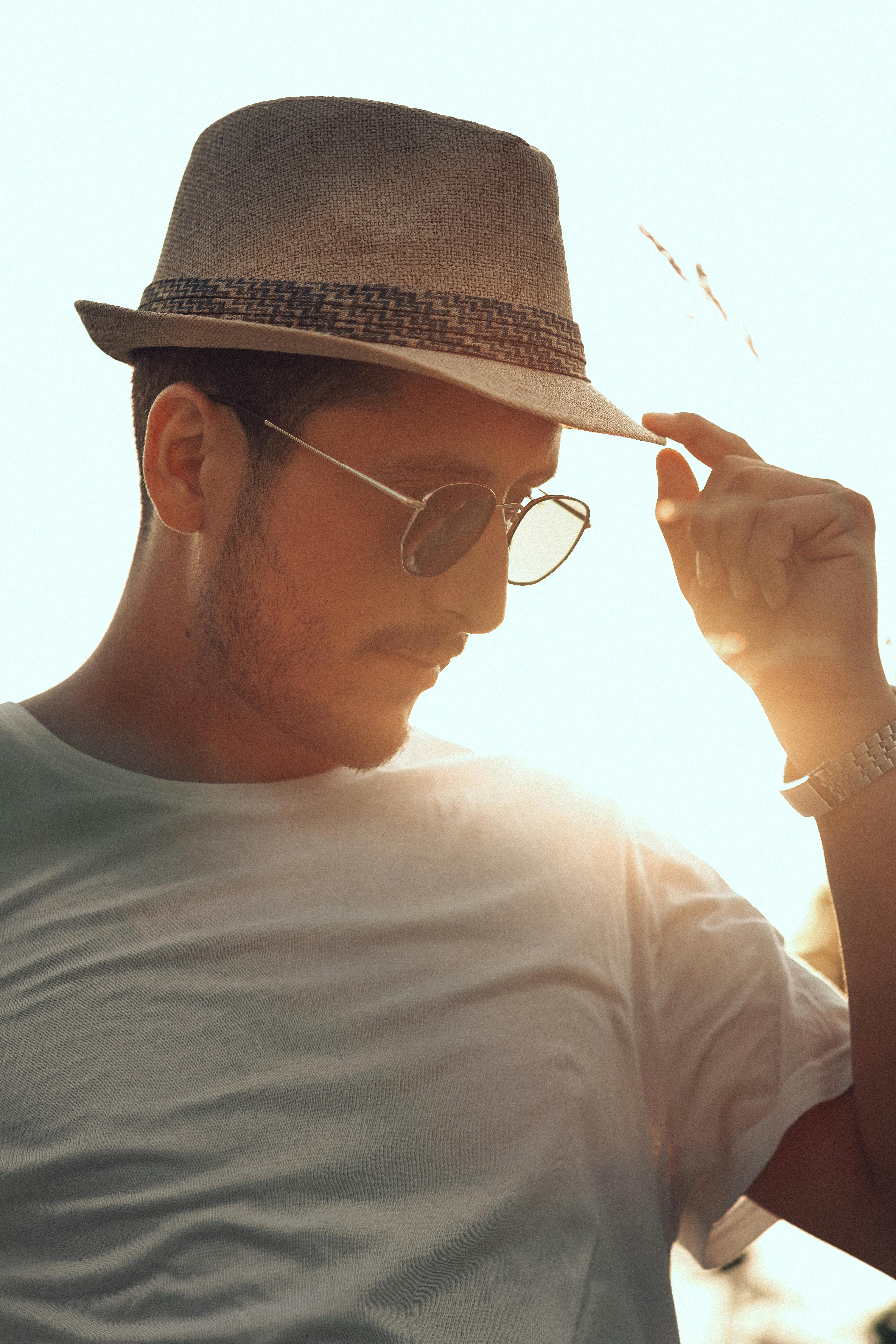 A man in a fedora and sunglasses poses confidently in the warm glow of sunset.