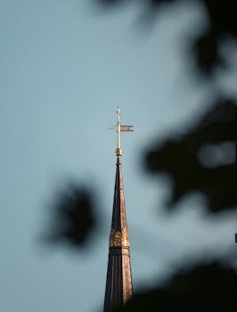 A beautiful church spire with a cross, framed against a clear blue sky.