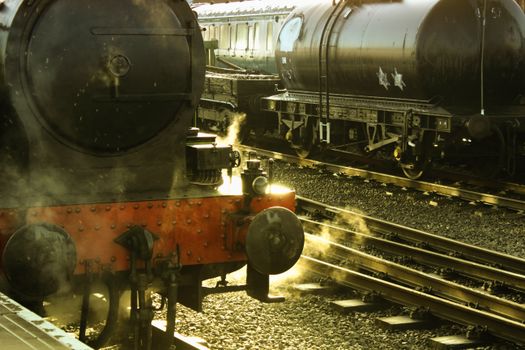 Steam locomotive releasing smoke at an outdoor train station with railroad tracks., free online jigsaw puzzle on JigsawPuzzlesFreeOnline.org