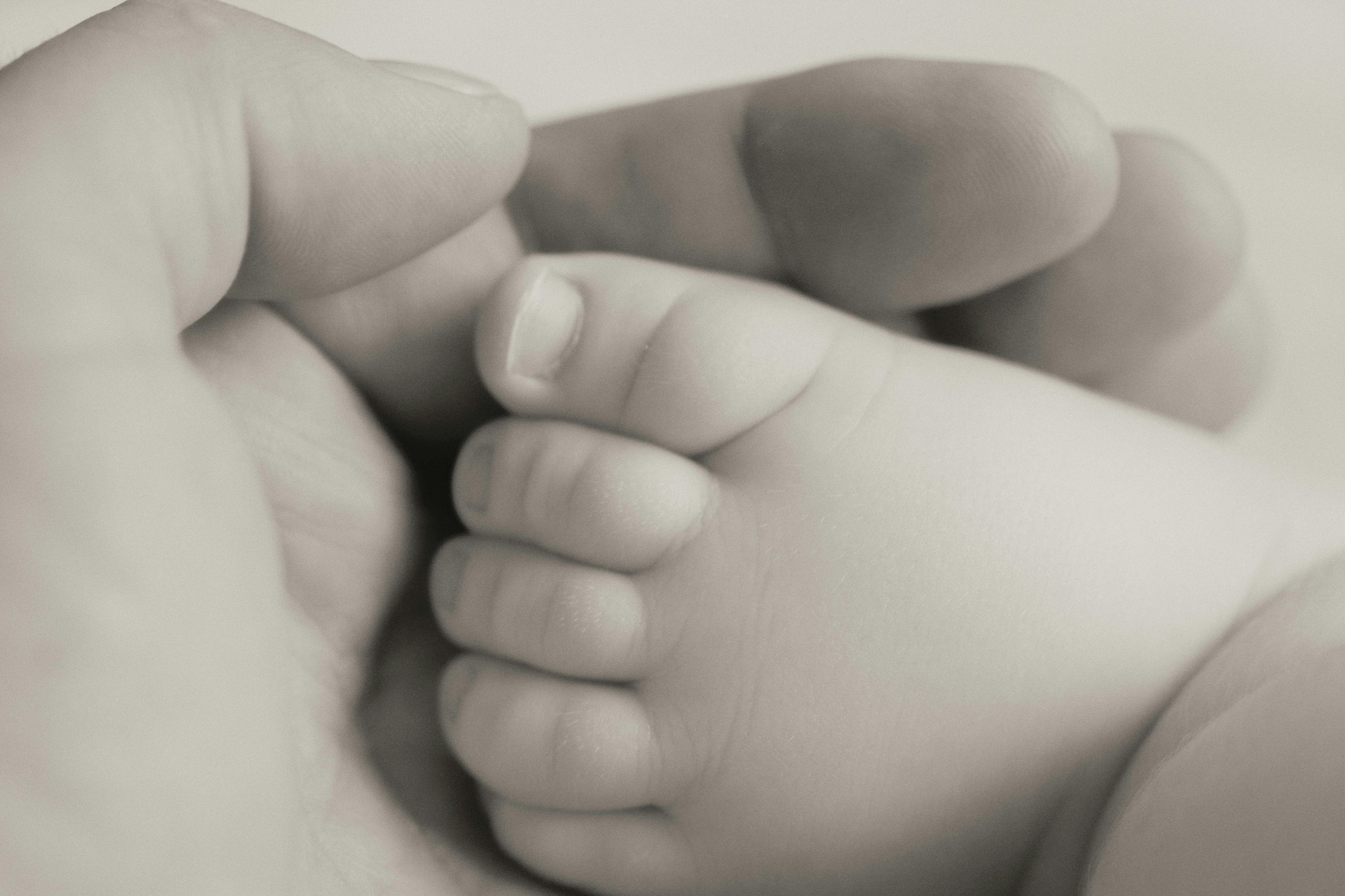 grayscale photography person holding baby s foot