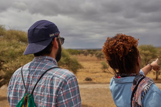 A man and woman explore the vast savanna under a looming cloudy sky.