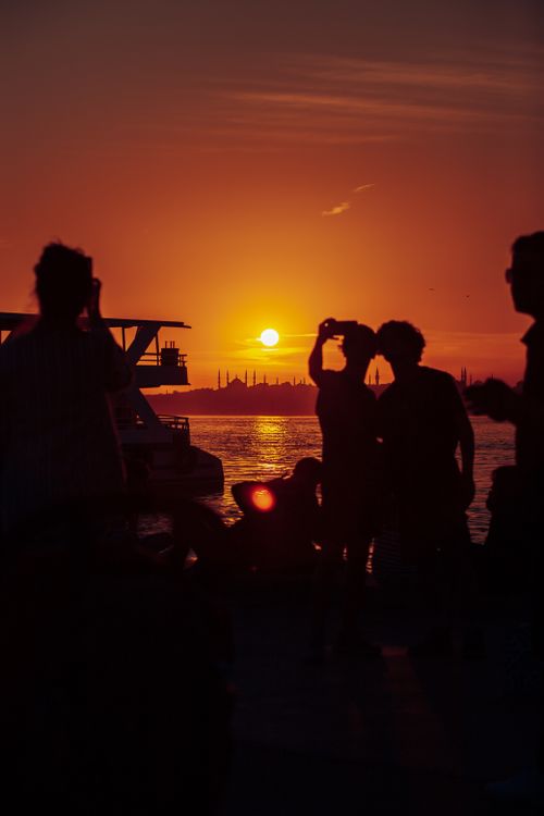 Free Silhouetted figures enjoy a vibrant sunset over the sea, capturing a serene moment of leisure. Stock Photo