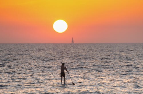 Man Standing While Paddling on Sea during Sunset