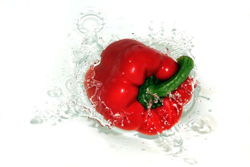 Free A fresh red bell pepper creating a dynamic splash in the water against a white background. Stock Photo
