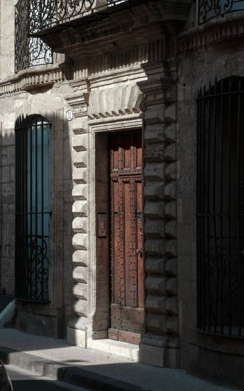 Free A sunlit view of a historic facade featuring an ornate wooden door and wrought iron grills. Stock Photo