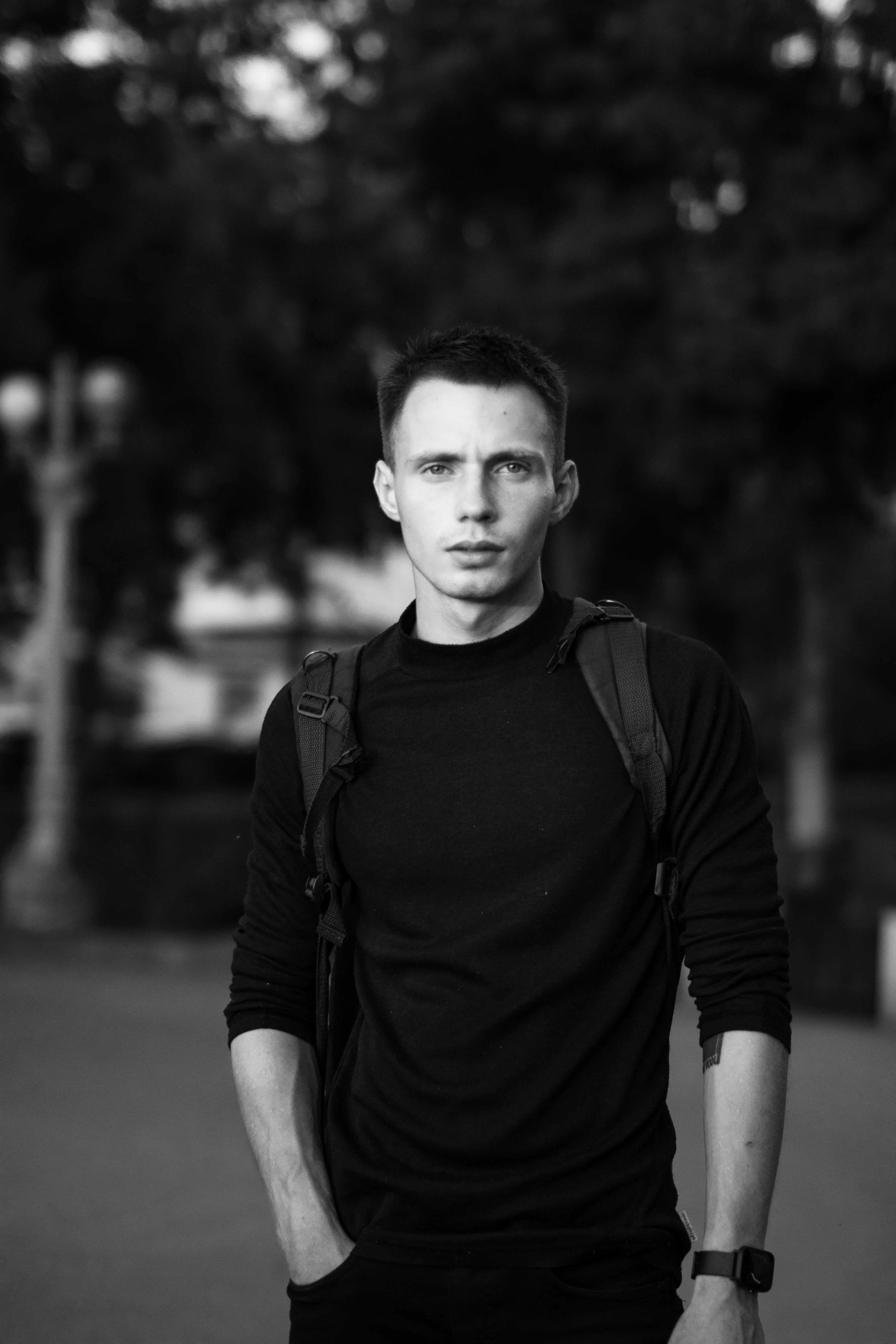Monochrome portrait of a young man in a black sweatshirt standing outdoors.