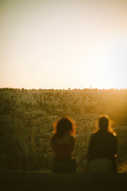 Free People Sitting and Watching Sun Setting Behind a Hill  Stock Photo