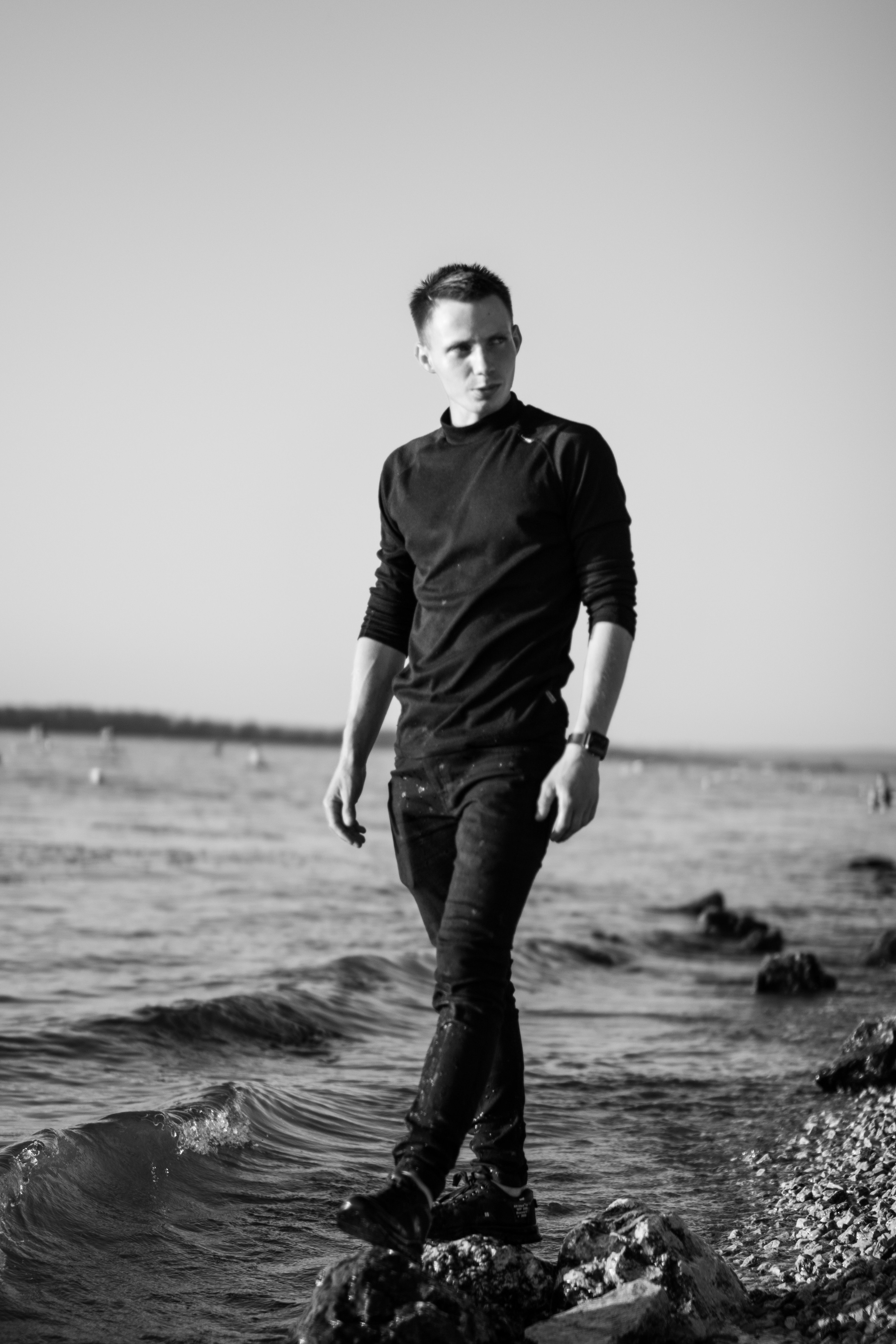 Stylish black and white portrait of a man walking along a rocky seaside, evoking a calm and reflective mood.