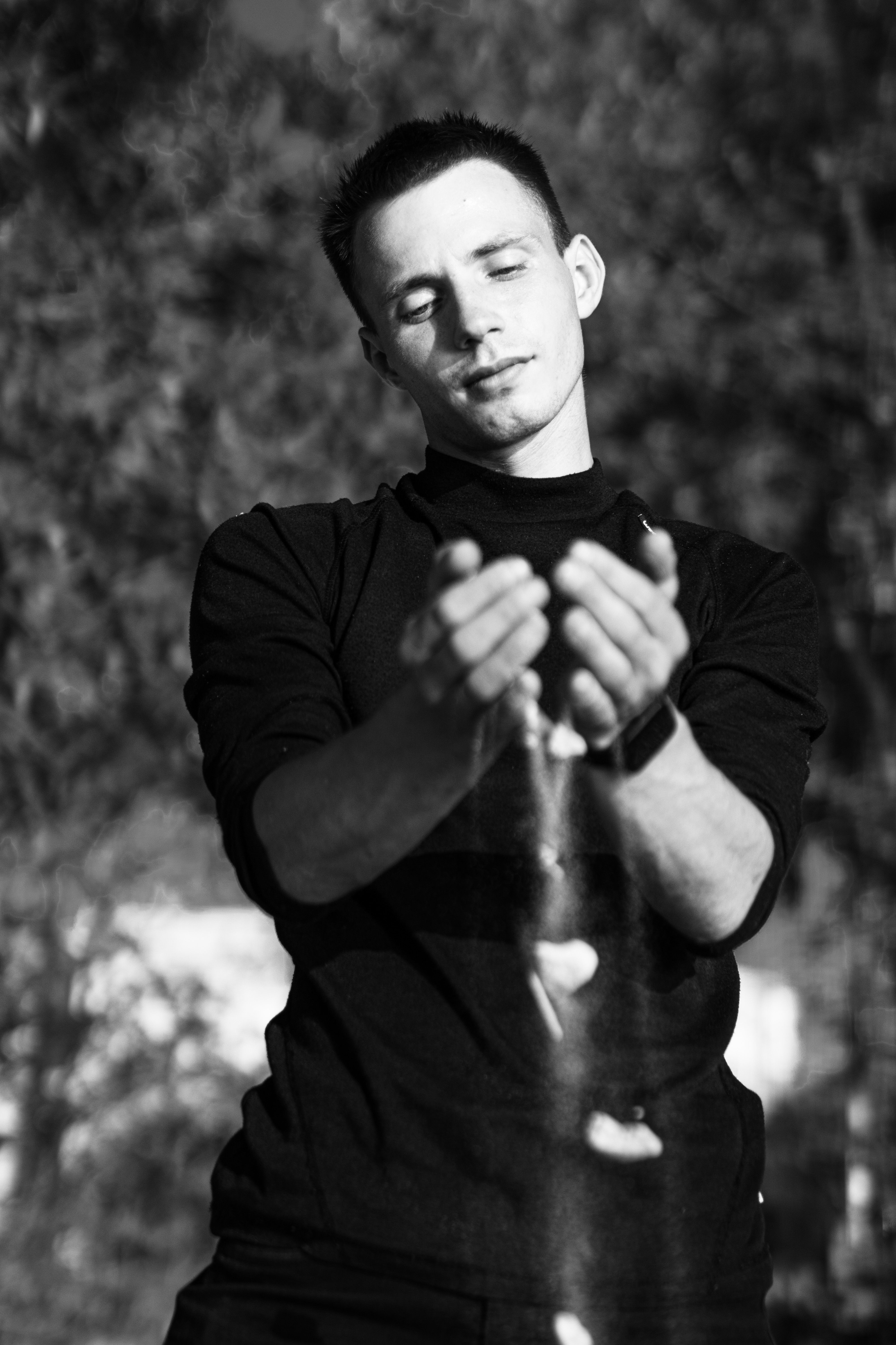 Monochrome photo of a man letting sand fall through his hands outdoors.