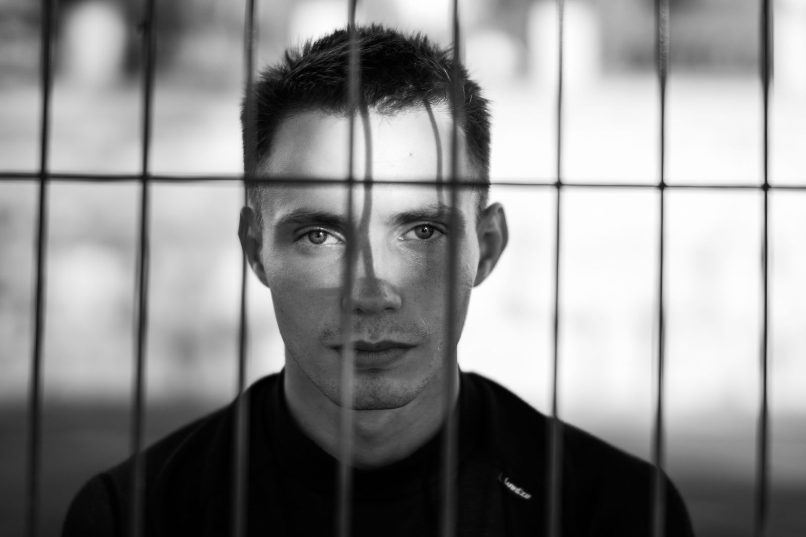 Man in black crew-neck shirt behind fence