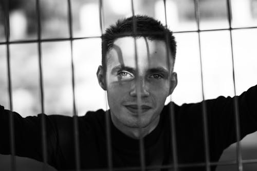 Grayscale Photo of a Man Behind Fence