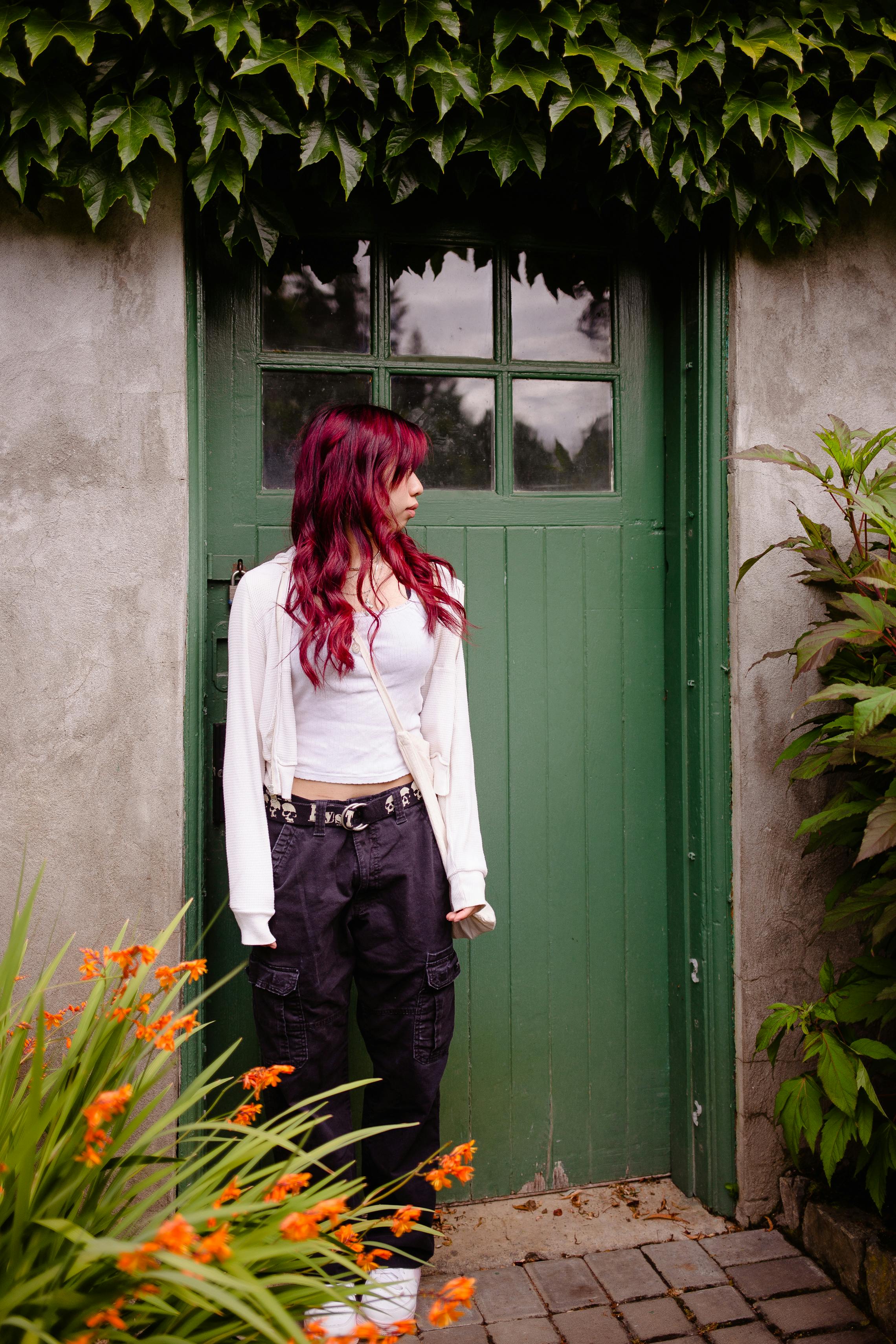 girl with dyed red hair standing in front of green front door