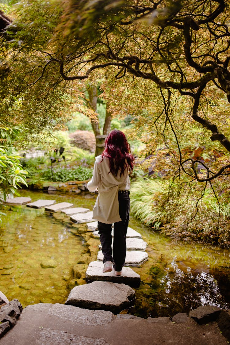 Back View Of A Young Woman Walking On Stepping Stones 