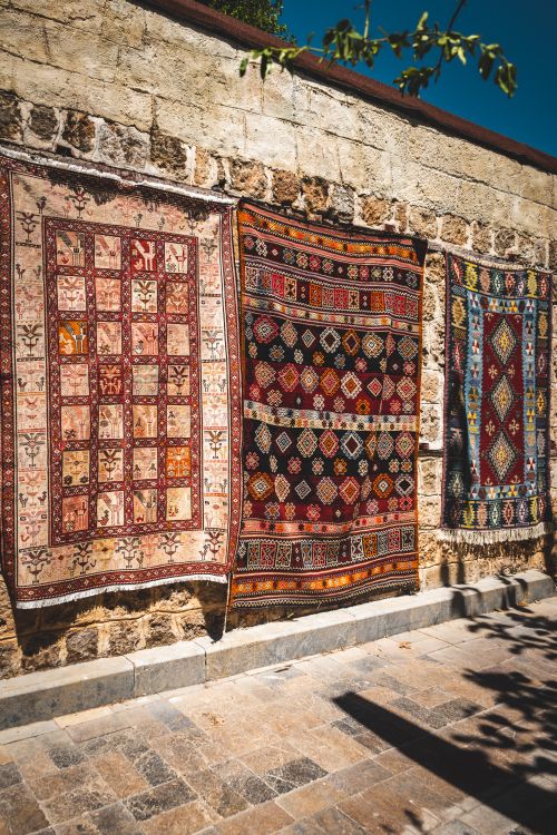 Free Vibrant carpets with intricate patterns hanging on a stone wall under bright sunlight. Stock Photo