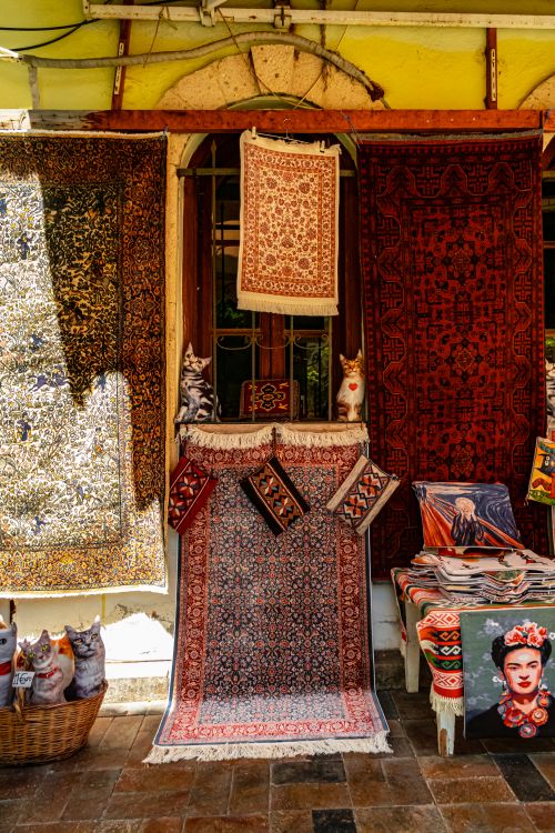 Free A vibrant display of rugs and figurines at a market stall, showcasing intricate designs and patterns. Stock Photo